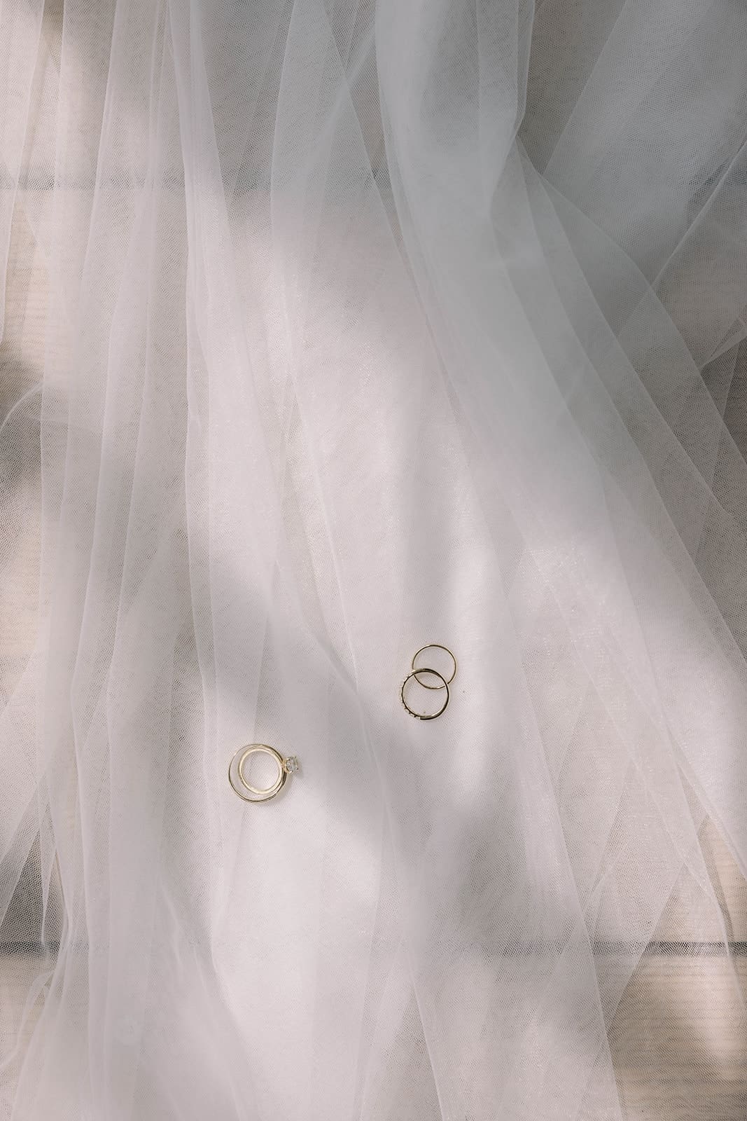 A photo of wedding rings laid on a veil in the sun by Tom Thornton Photography. 