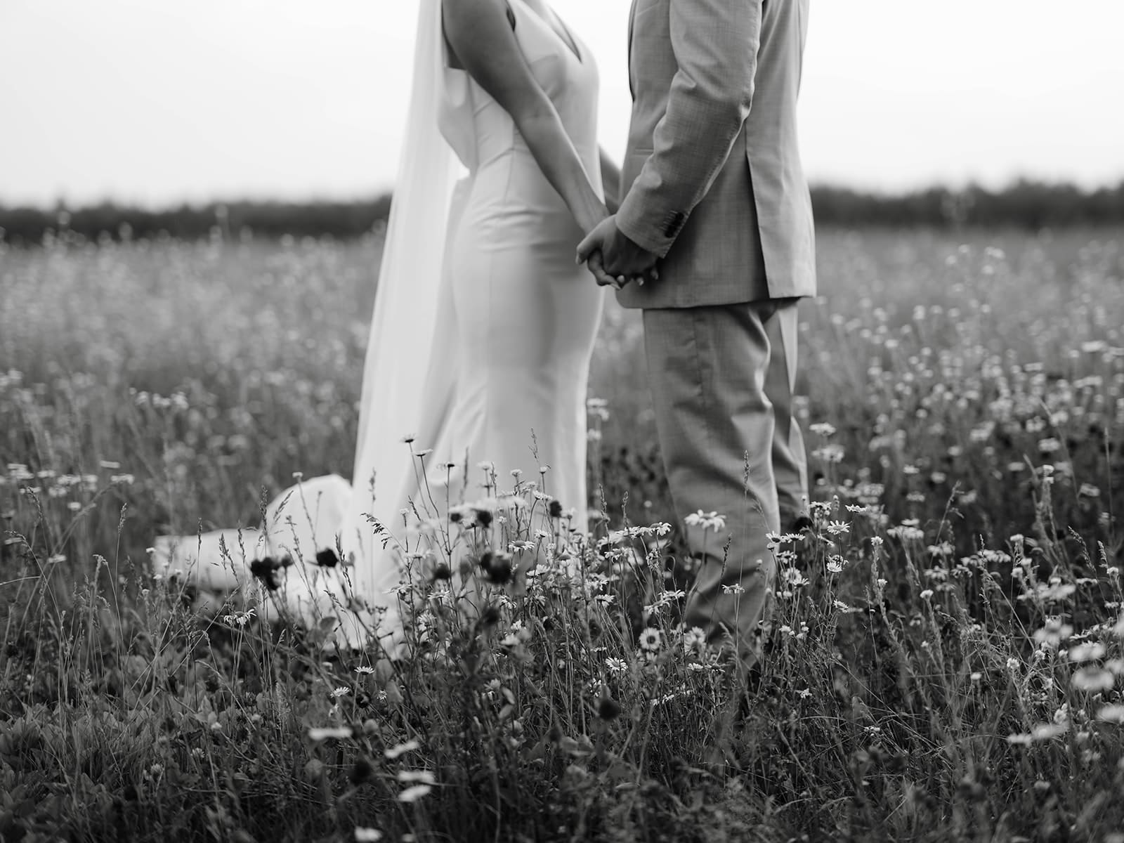 Bride and groom hand-holding photo in a flower field at an Ivory North wedding in Mora, MN. 