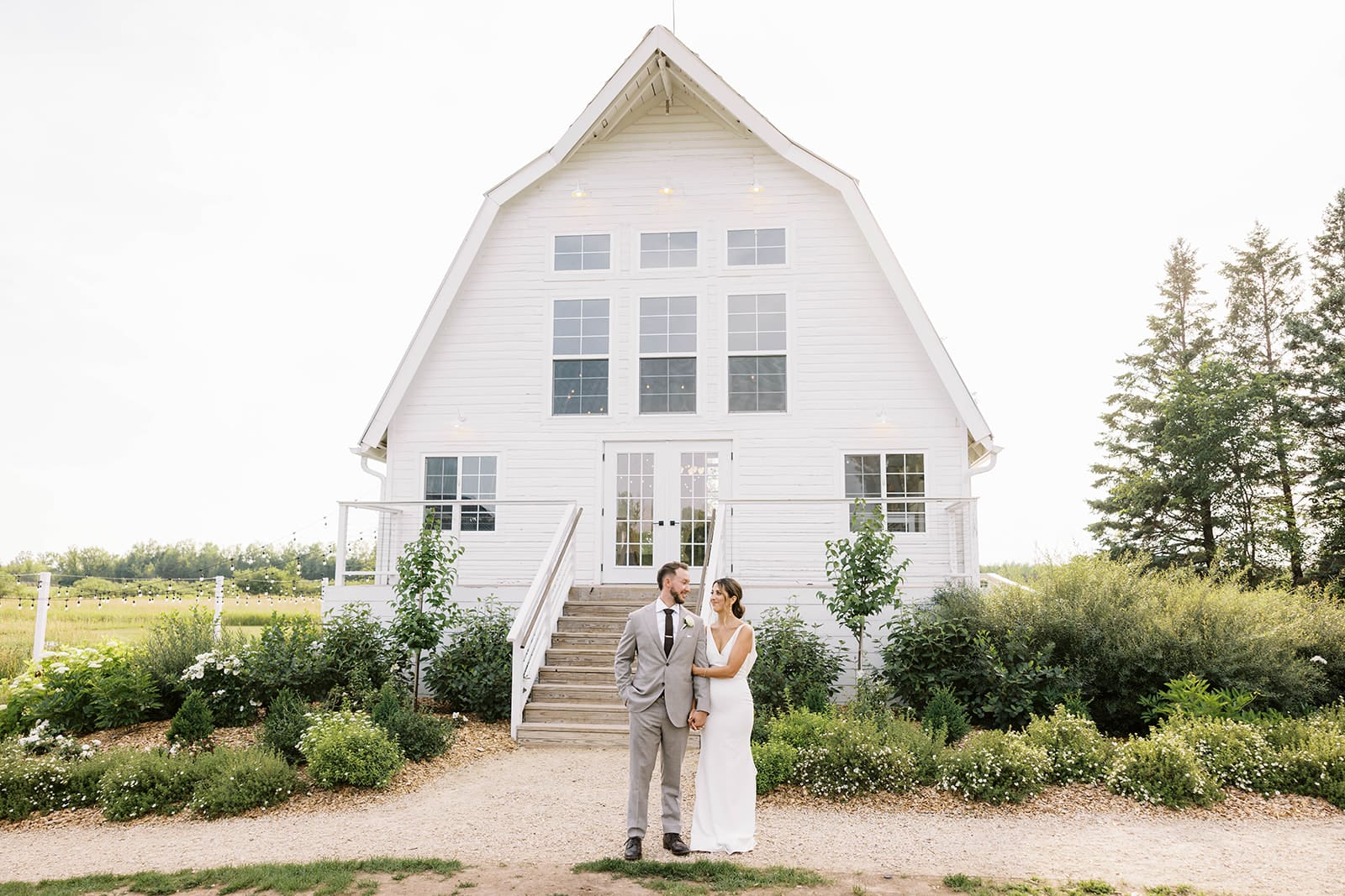 Bride and groom posing for a photo with the white barn at ivory north co wedding venue. Tom Thornton Photography. 