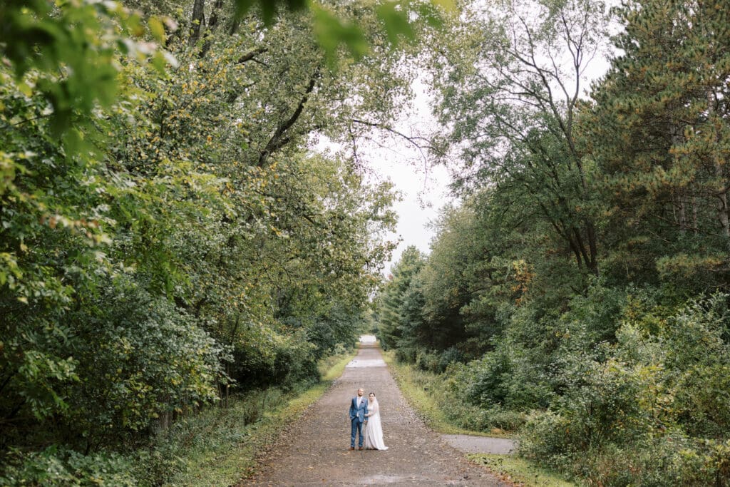 Wide photo of a bride and groom out for a walk in the trees at the Outing lodge wedding venue in Stillwater, MN at Golden hour. 