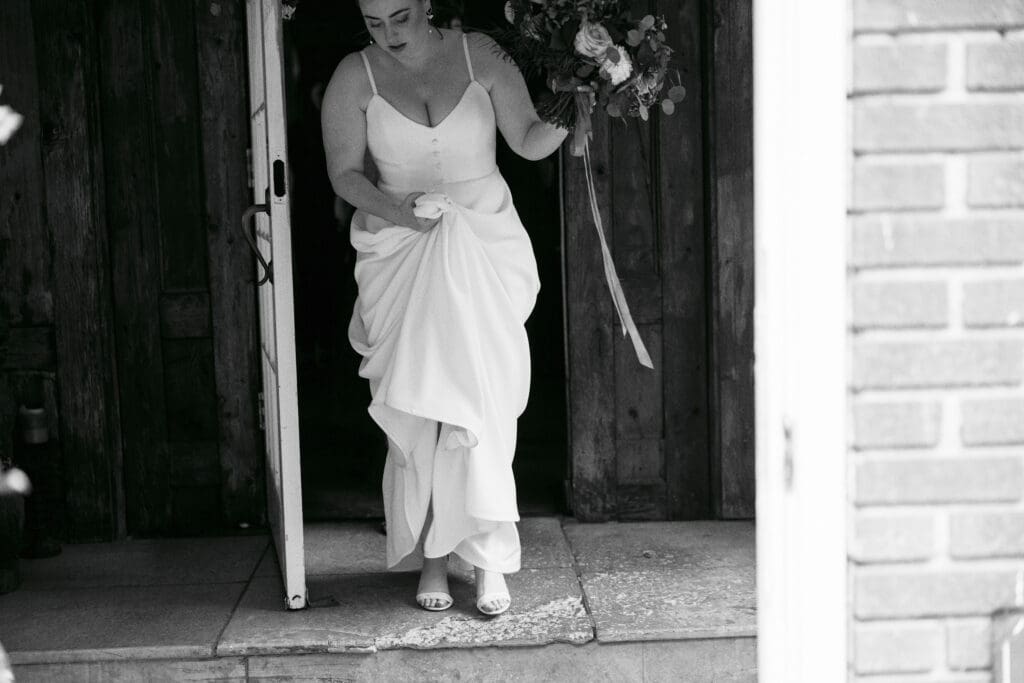 Bride holding her dress and flowers as she walks out of the Outing lodge to go to the first look with the groom. 