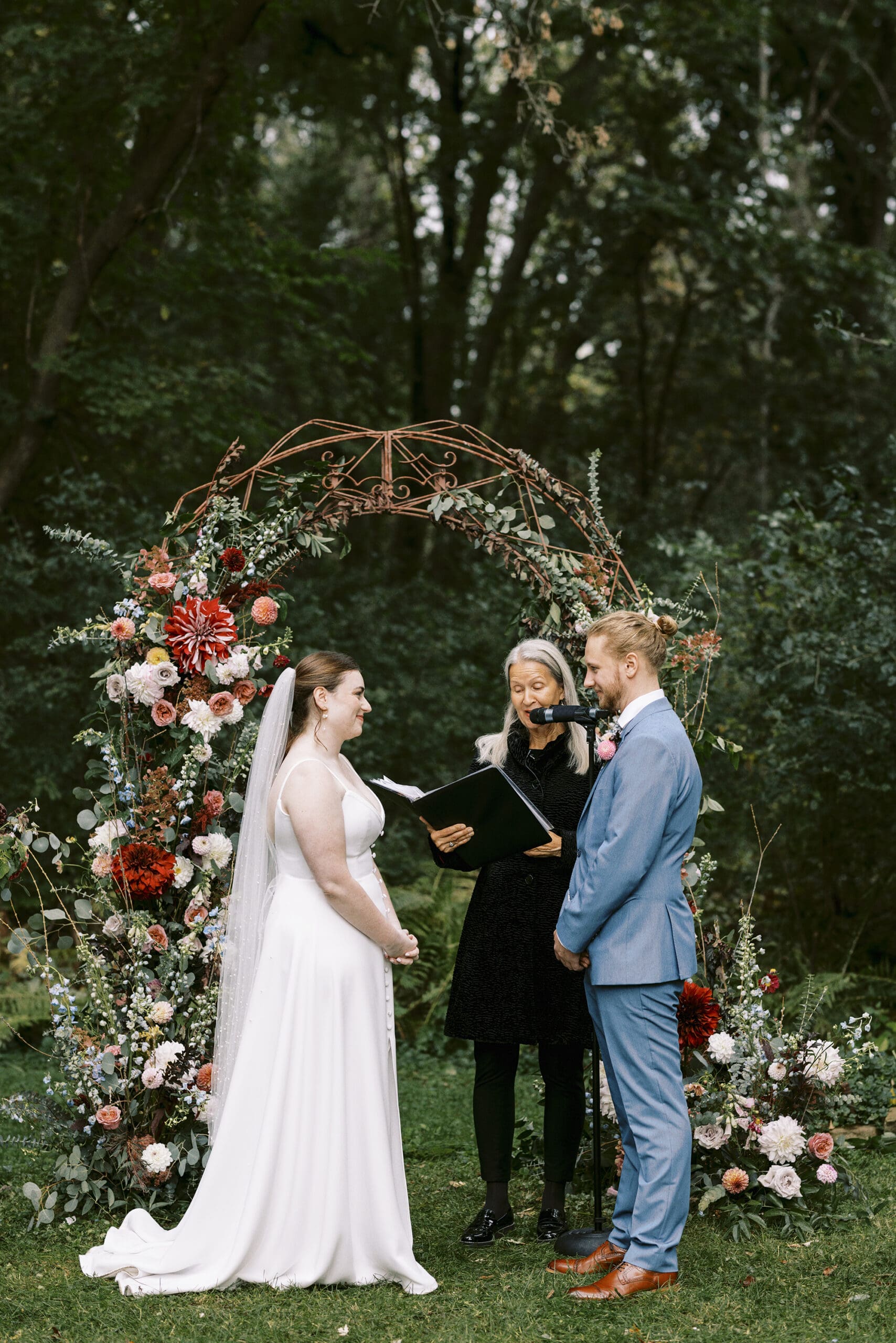 Bride and Groom under the floral arch during the rainy garden wedding ceremony at the Outing Lodge in Stillwater, Minnesota. 