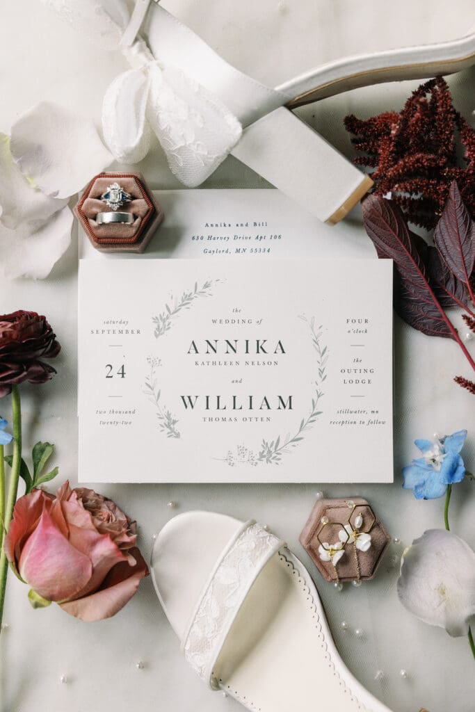 A close-up photo of the couple's wedding invitation and florals displayed on a marble table at The Outing lodge in Stillwater, MN.  